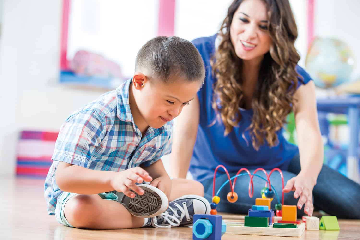 photo of young boy with Down Syndrome playing with colourful toys on floor with classroom assistant)