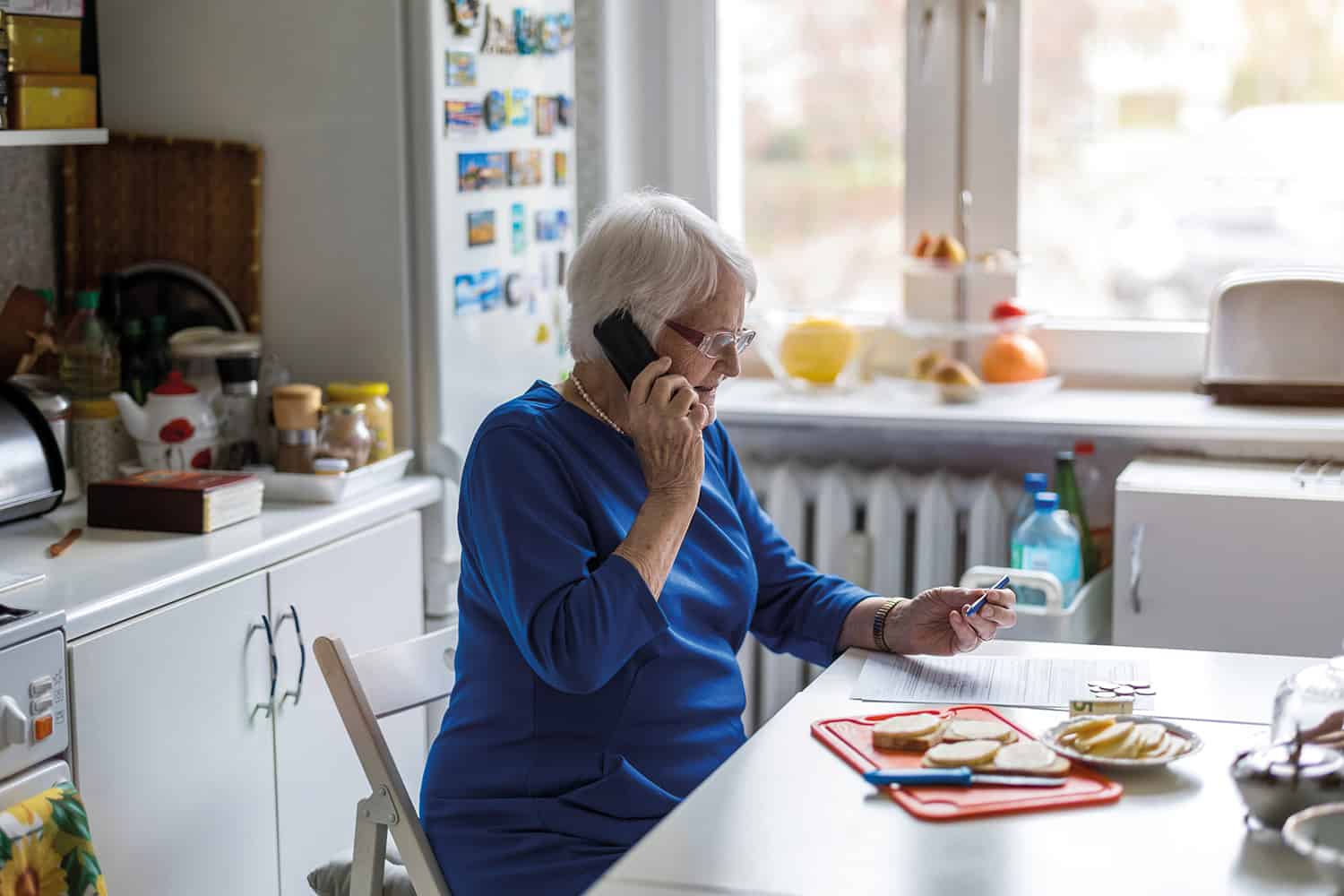 An elderly lady sat at the kitchen table on the telephone.