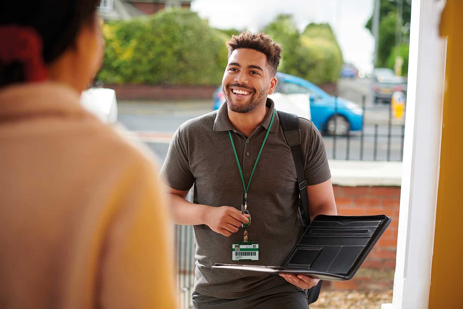 A black, male, housing officer speaking to a woman at the front door.