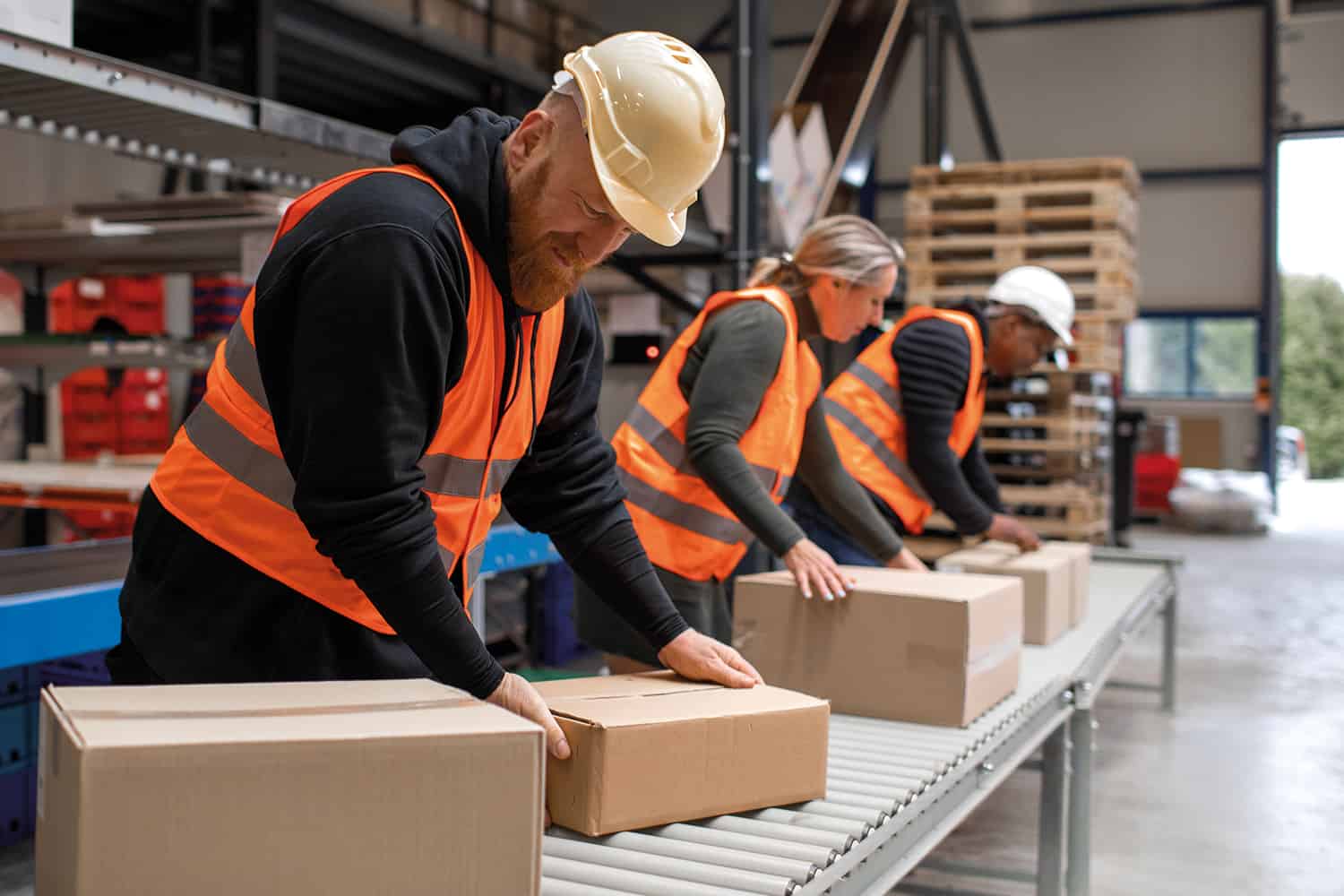 : three people in high-vis jackets checking parcels on a production line