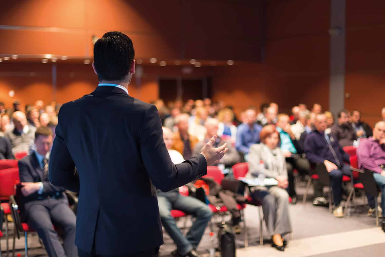 man with back to camera speaking to audience at conference