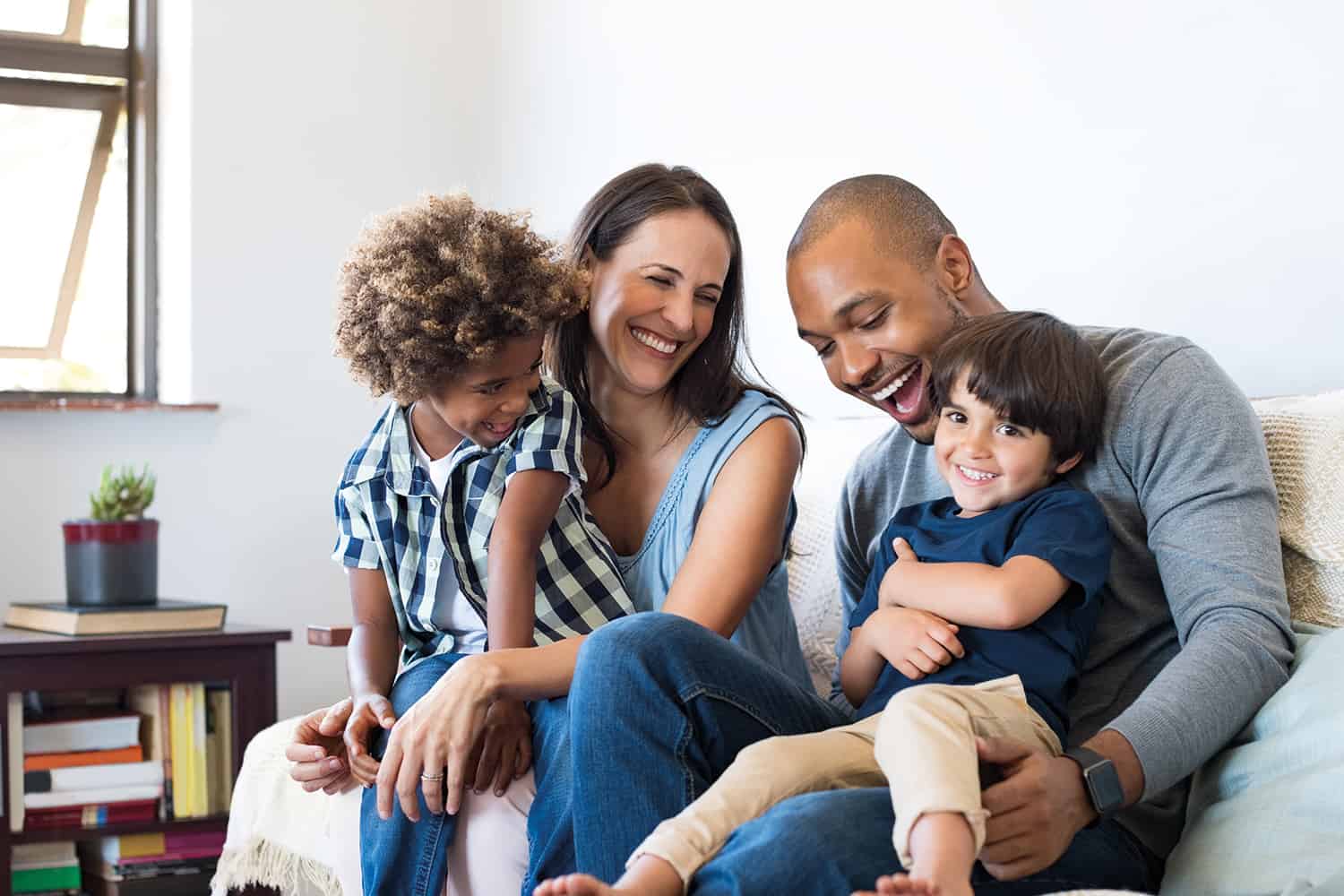 Two parents and their two young children sitting together on the sofa smiling