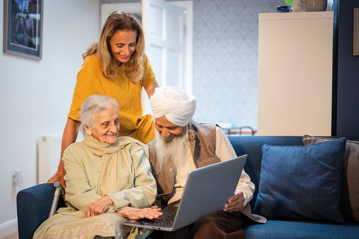 photo of older Sikh man and woman on sofa using laptop to connect socially