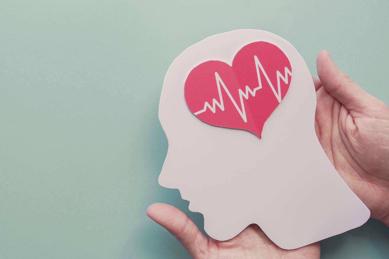 photo of hands holding a cut-out of a human head with a red heart where the brain goes.