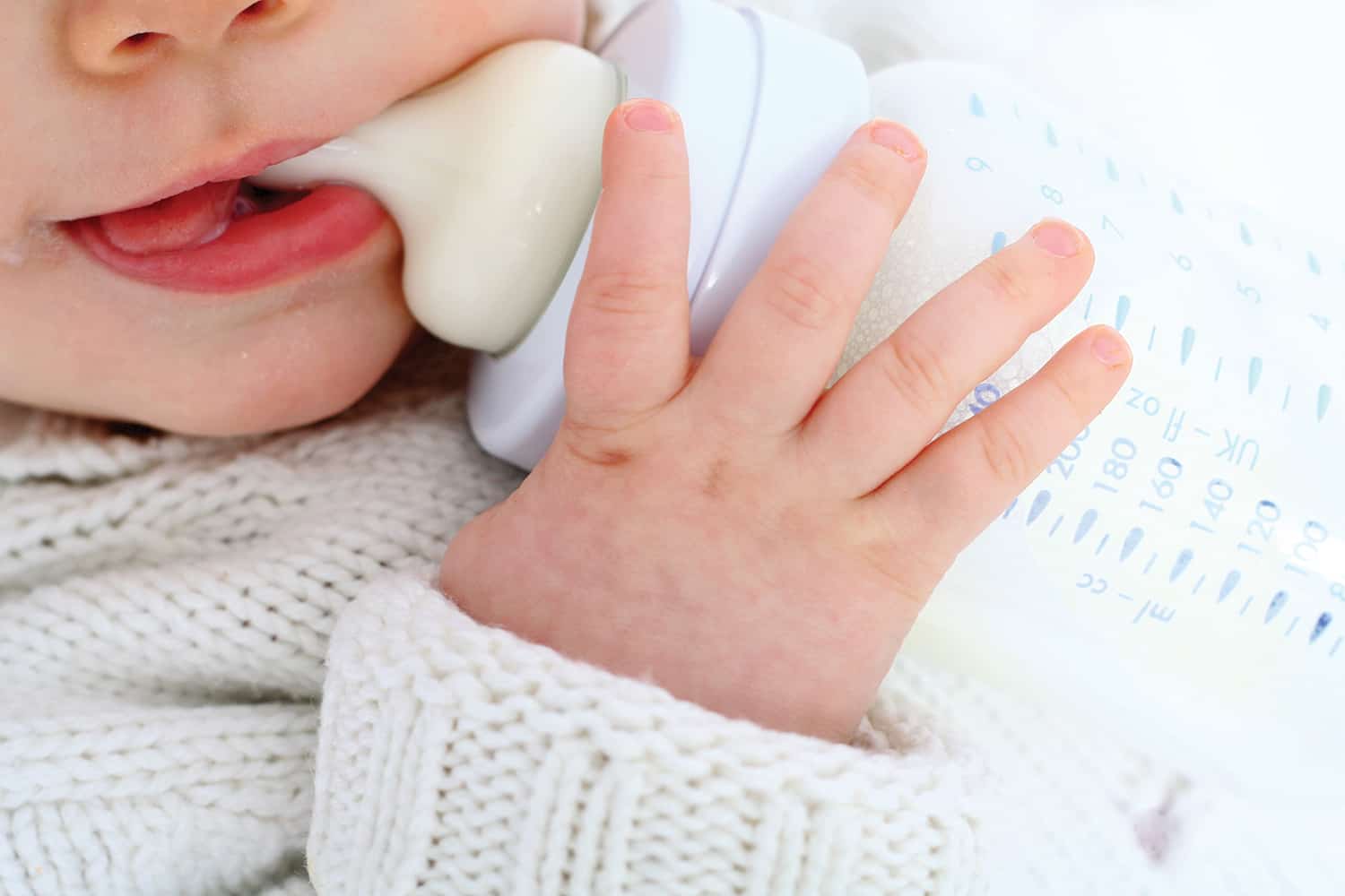 A baby holding a bottle of milk in the mouth.