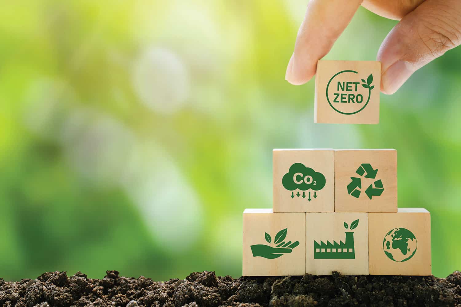 Fingers stacking wooden cubes with green symbols on them, including CO2, net zero and the recycling symbol