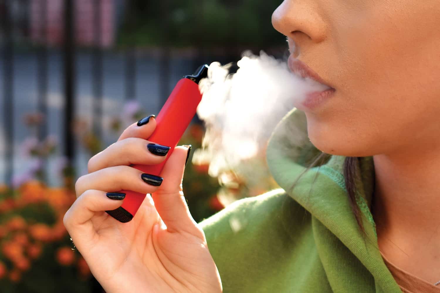 close-up of a woman holding a vape to her face and smoke coming out of her mouth.