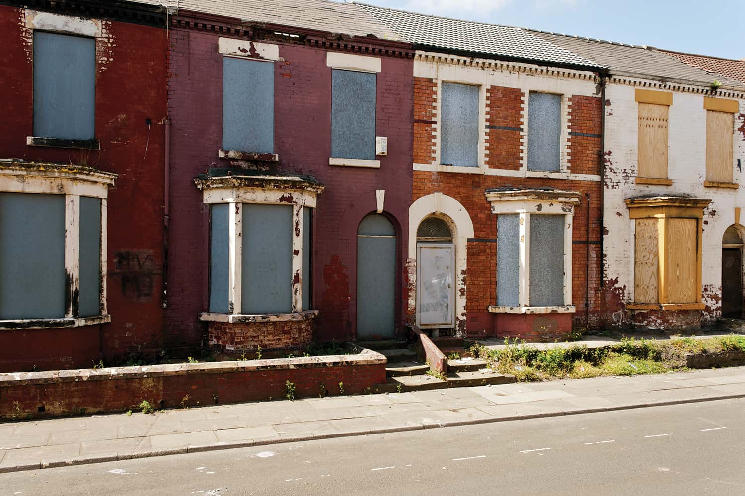 row of terraced red-brick houses with metal boards on doors and windows