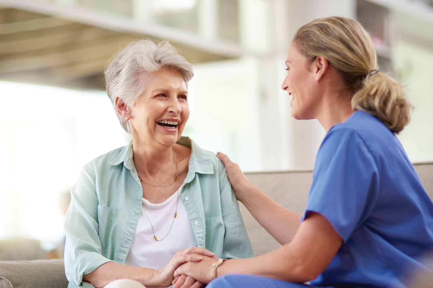 A nurse sitting with her hand on shoulder of an elderly woman.