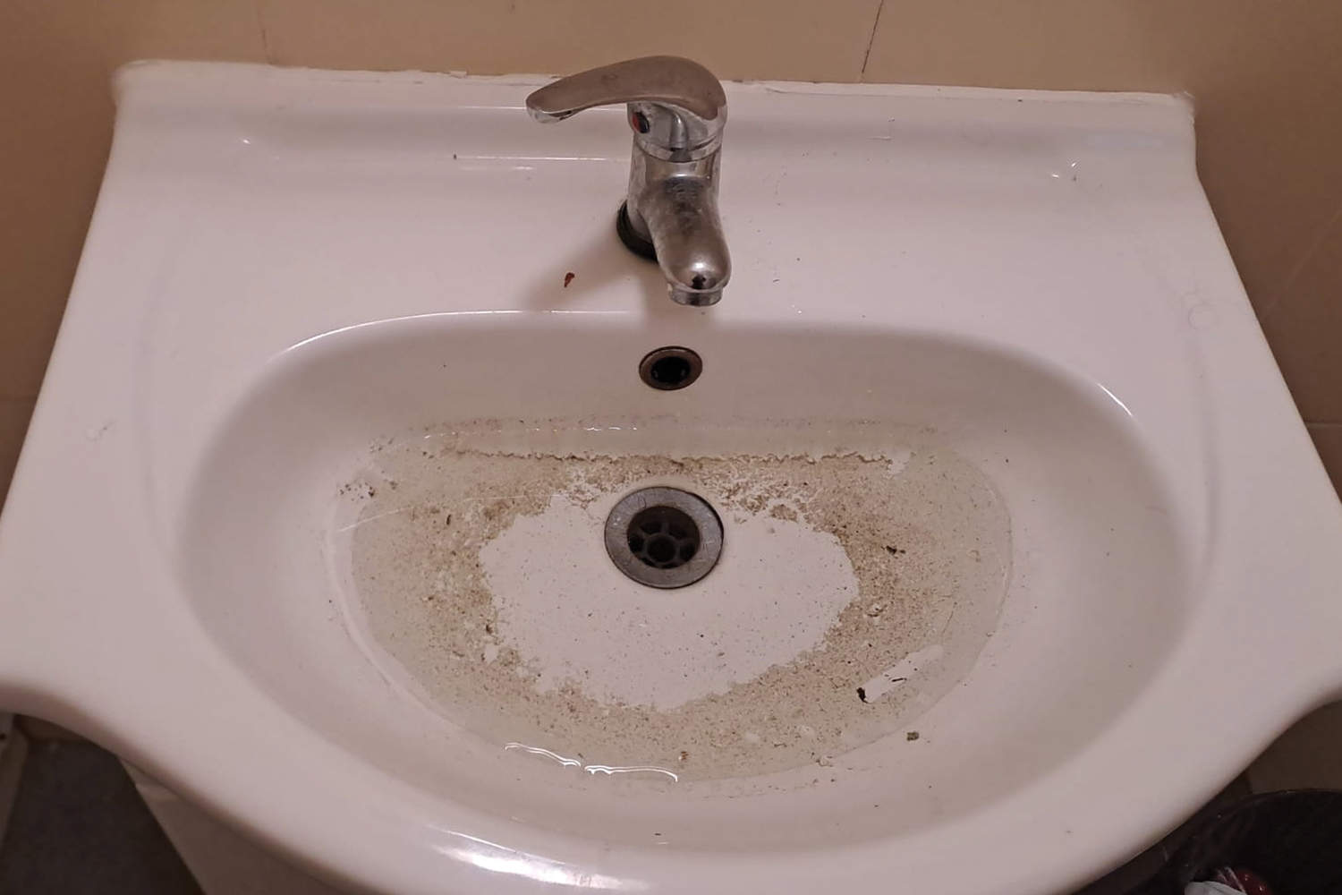 A bathroom sink with a layer of grime and dirt around the sink hole