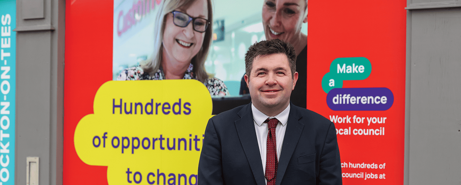 photo of Cllr Shaun Davies, LGA Chair, in front of a local government recruitment advert in Stockton-on-Tees,