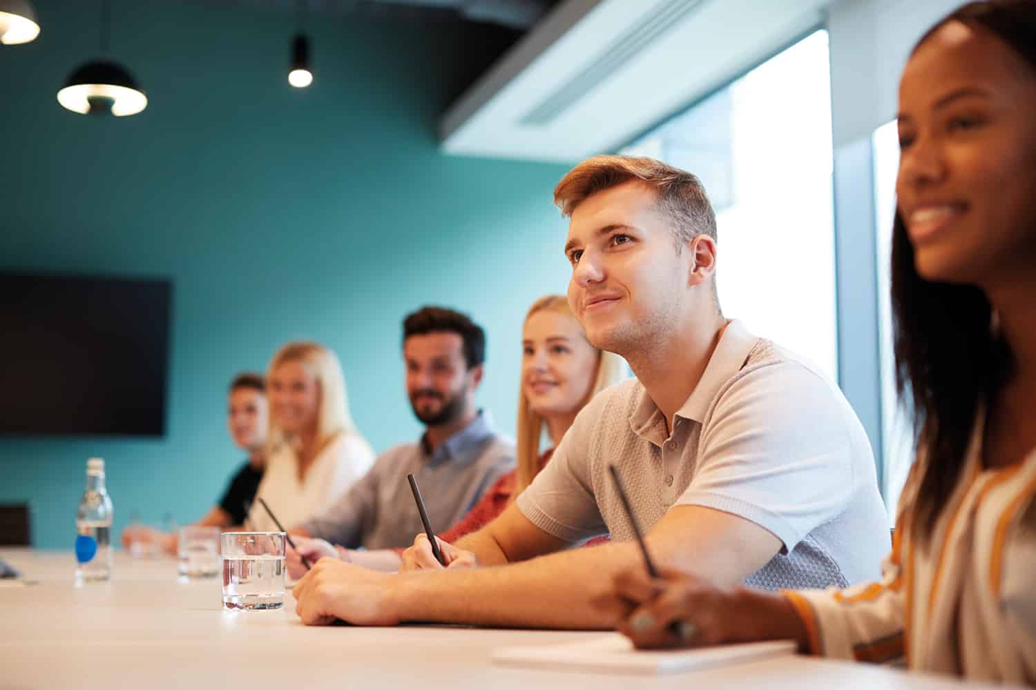 photo of mixed group of six young people at table smiling and looking up towards out-of-shot speaker or trainer