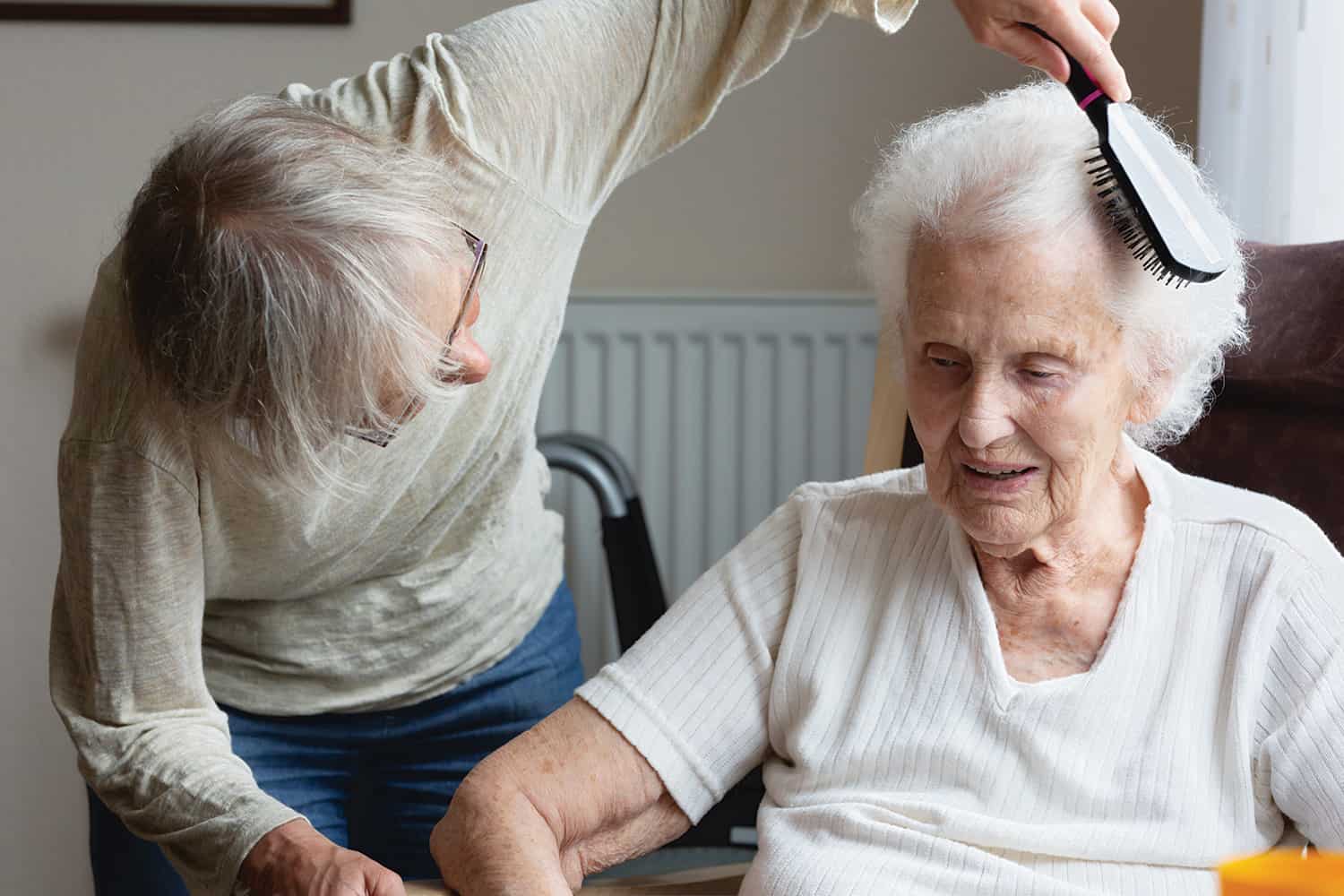 An elderly lady having her hair brushed by a relative