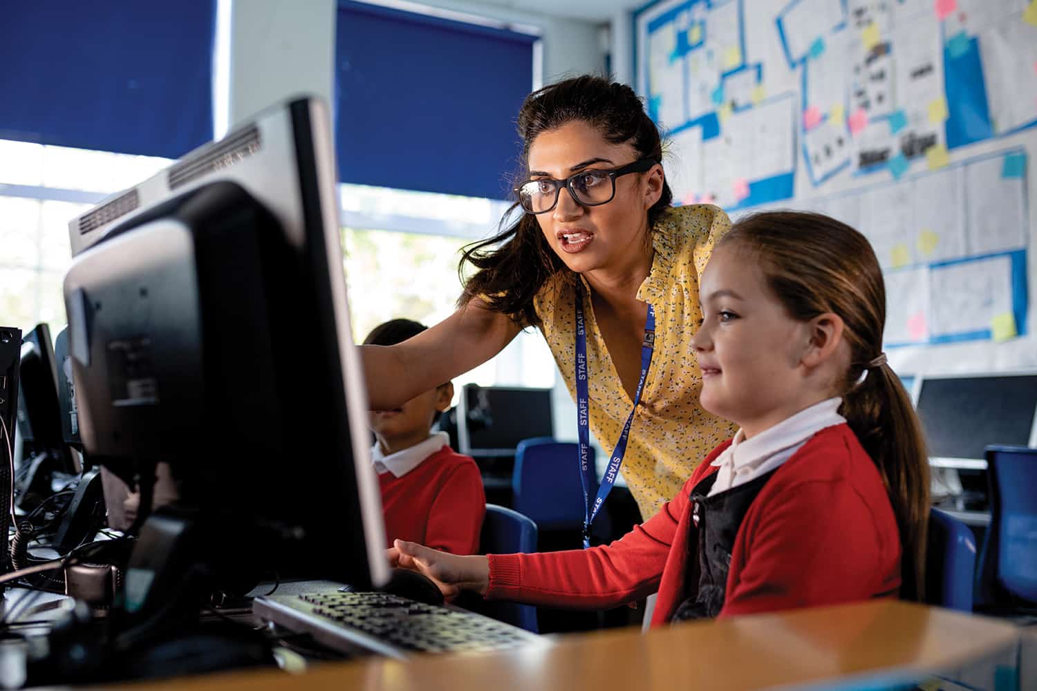A teacher showing a young pupil something on a computer monitor
