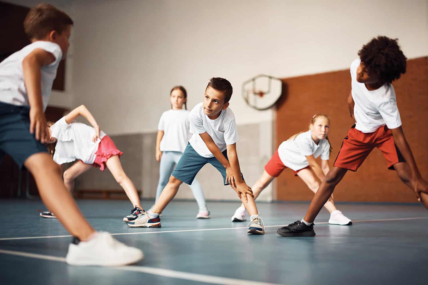 A group of young children doing a warm up stretch in a school gymnasium