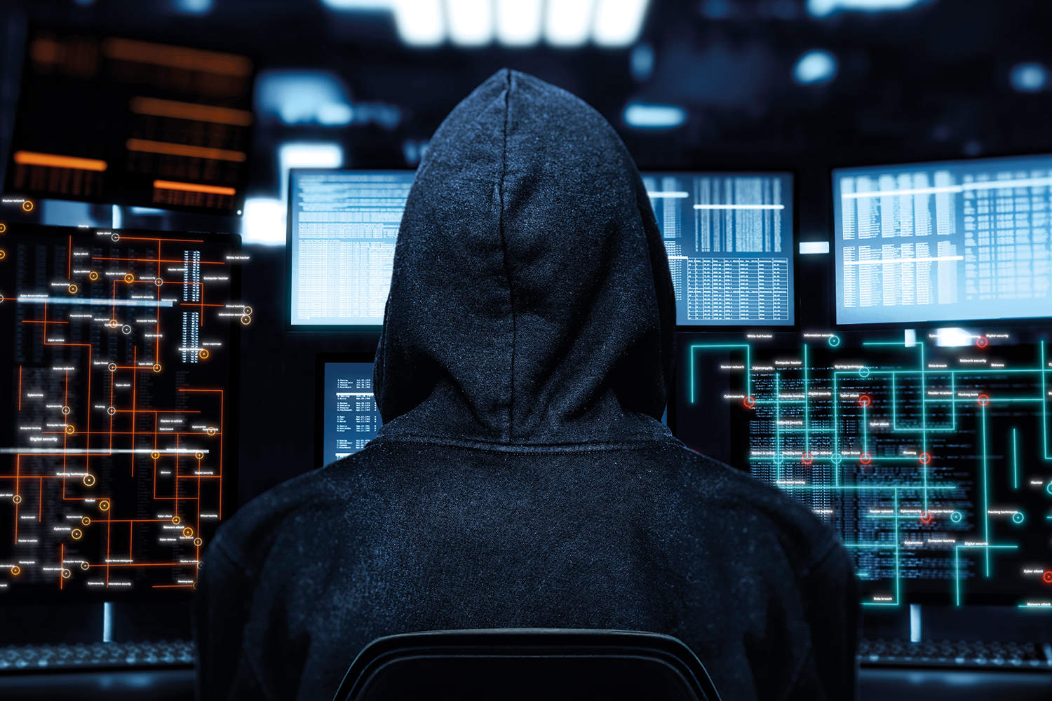 photo from behind of hooded person sat in front of several computer screens, overlaid with grid-like graphics of connecting computer systems