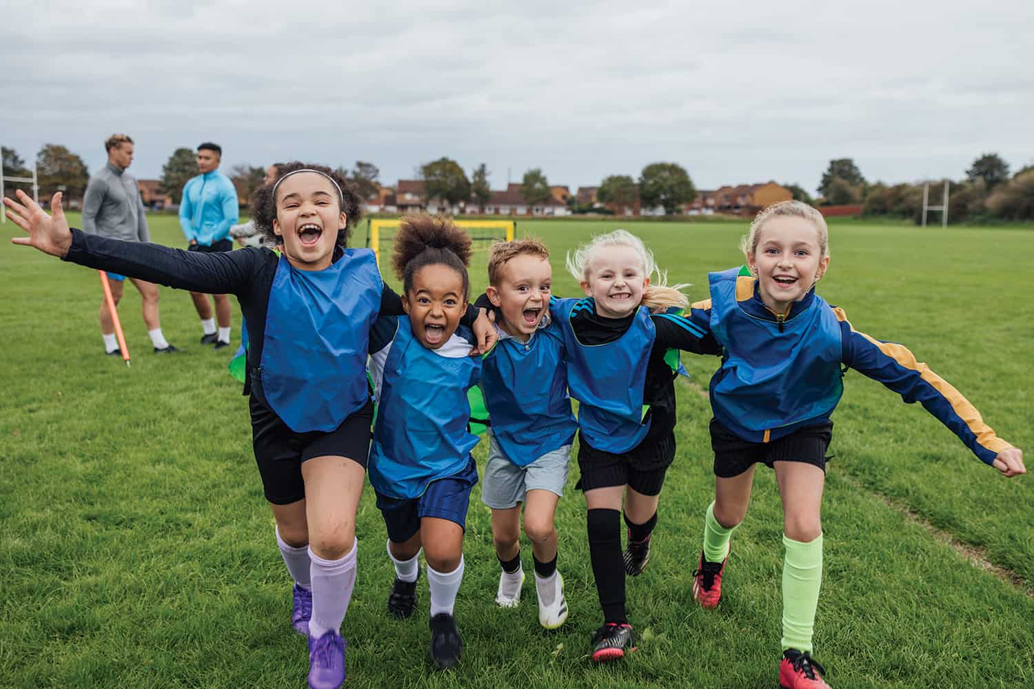 hoto 1 of four exuberant, grinning primary school-age girls and a boy with arms over each other’s shoulders running at camera with football coaches in background; photo 2 of older woman using stretch band in exercise class