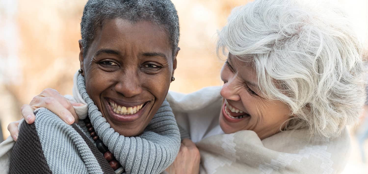 photo of two older women, one white, one black, hugging and smiling