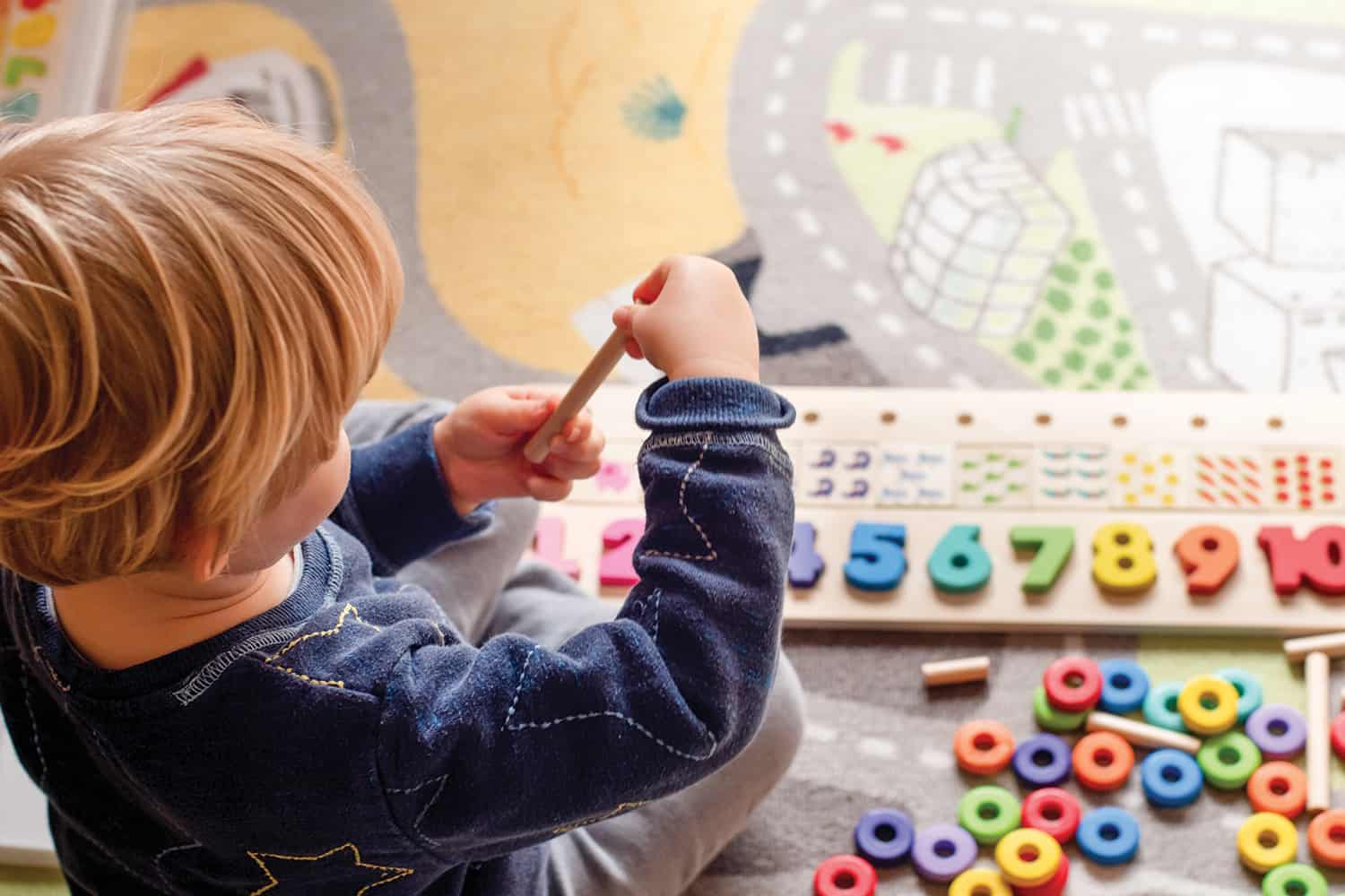 photos of a smiling childcare worker watching two children painting, and a view from behind and above of a young boy playing with a colourful number board