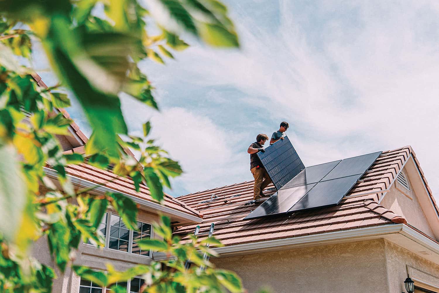 Pic: photo of two workmen installing solar panels on roof of house.