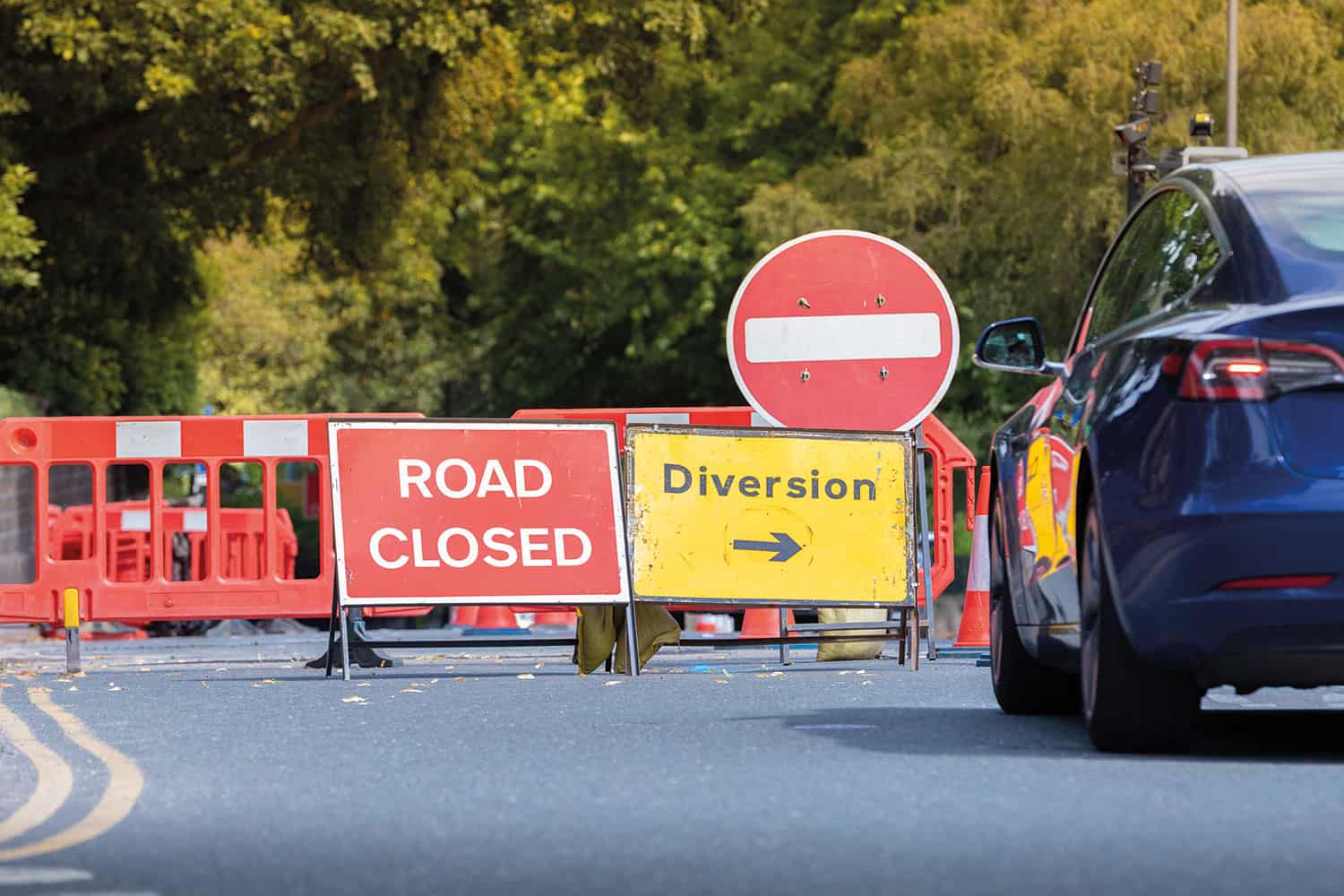 photo of car approaching red ‘road closed’ and yellow ‘diversion’ signs in front of red barriers around utility works