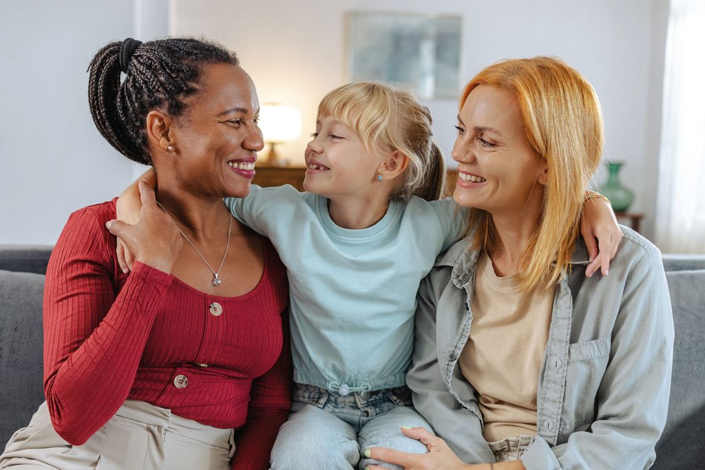 a young girl hugging female couple on sofa in front room