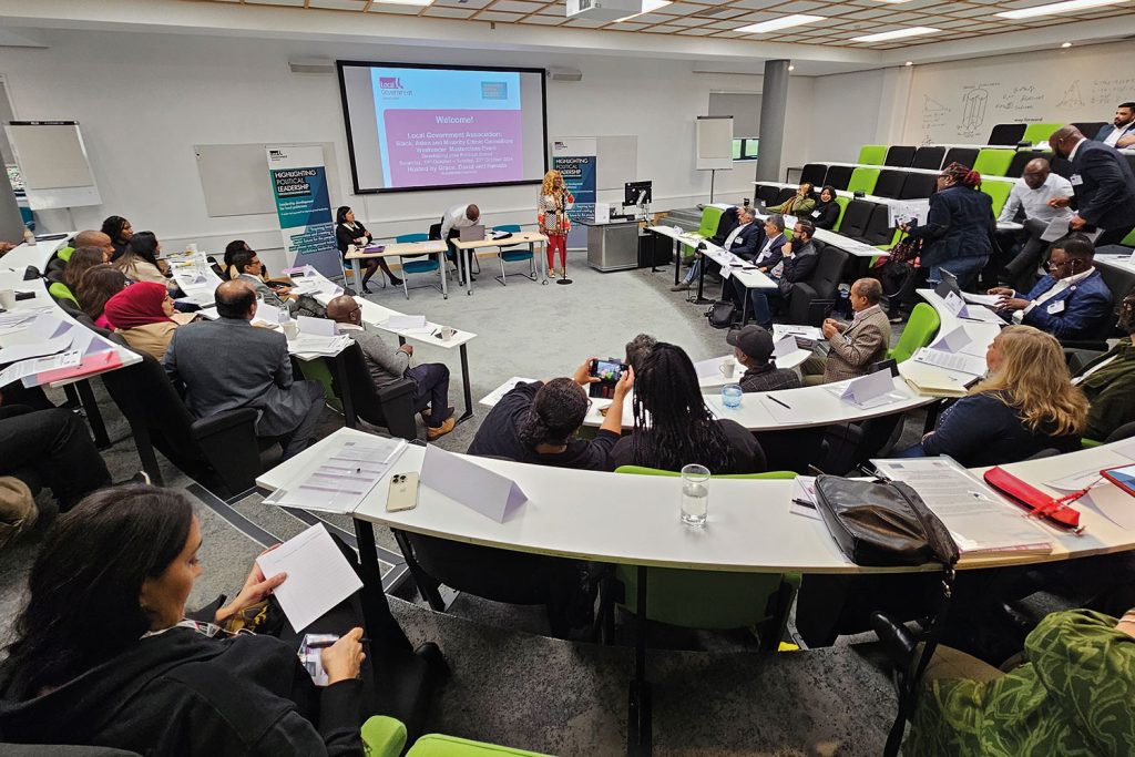smaller shot of delegates in a lecture room from the audience perspective looking towards speakers and a big screen