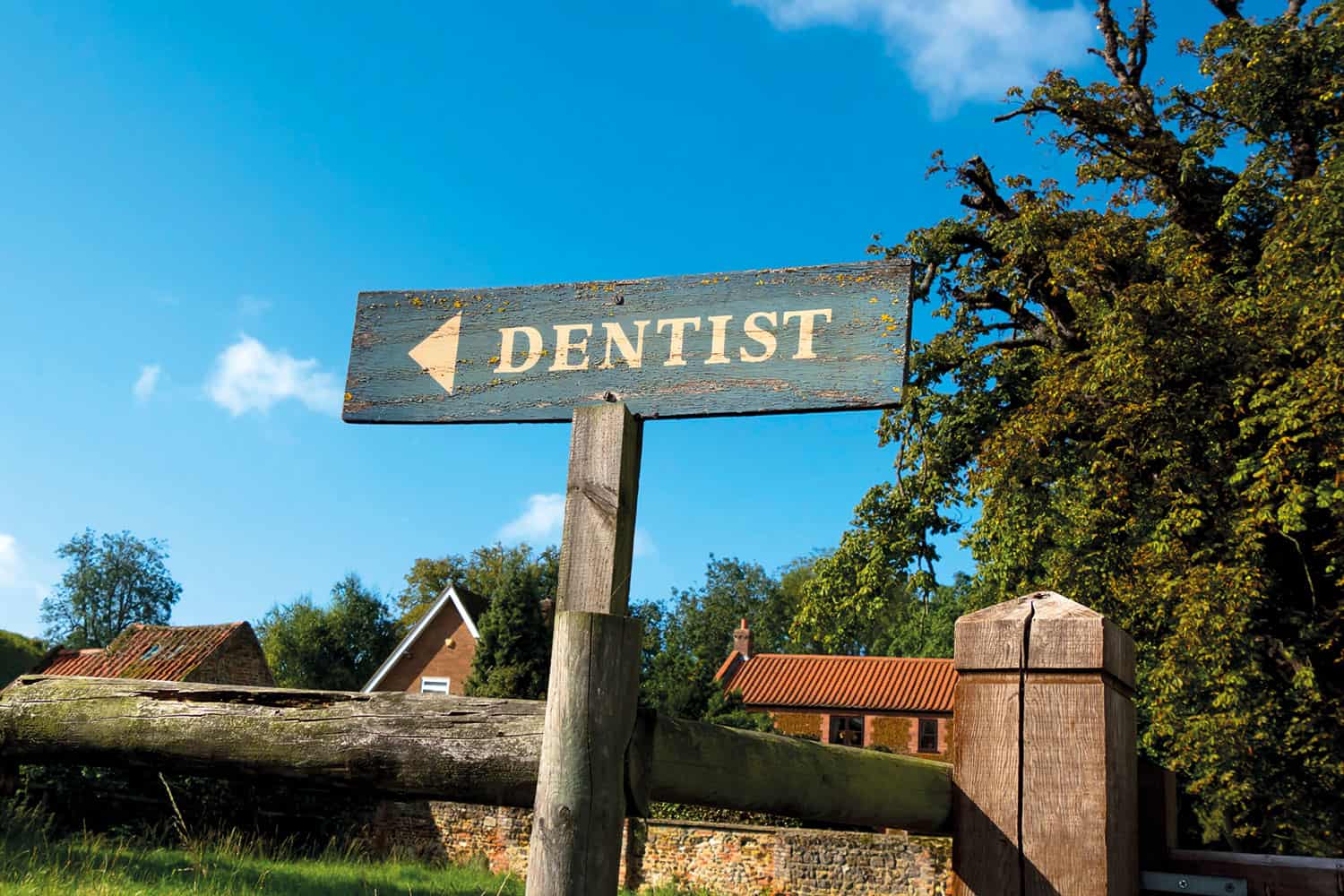 photo of wooden sign saying ‘Dentist’ pointing to the left, with a farm or rural houses in the near background)