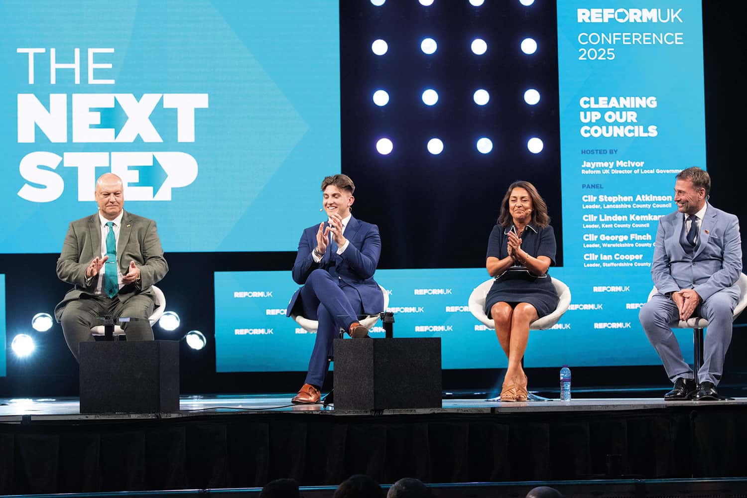 photo of panel discussion at the Reform UK Conference featuring (l to r) Cllr Ian Cooper (Staffordshire), Cllr George Finch (Warwickshire), Cllr Linden Kemkaran (Kent) and Cllr Stephen Atkinson (Lancashire), against a turquoise backdrop