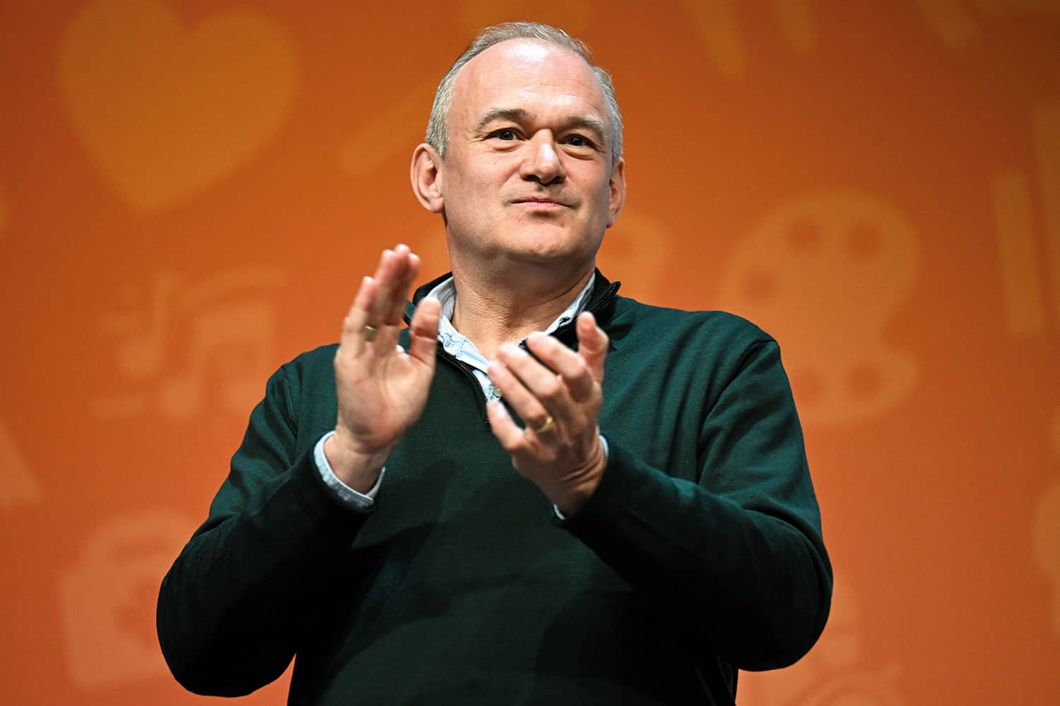 photo of Sir Ed Davey, Leader of the Liberal Democrats, applauding during a question-and-answer session, against an orange backdrop
