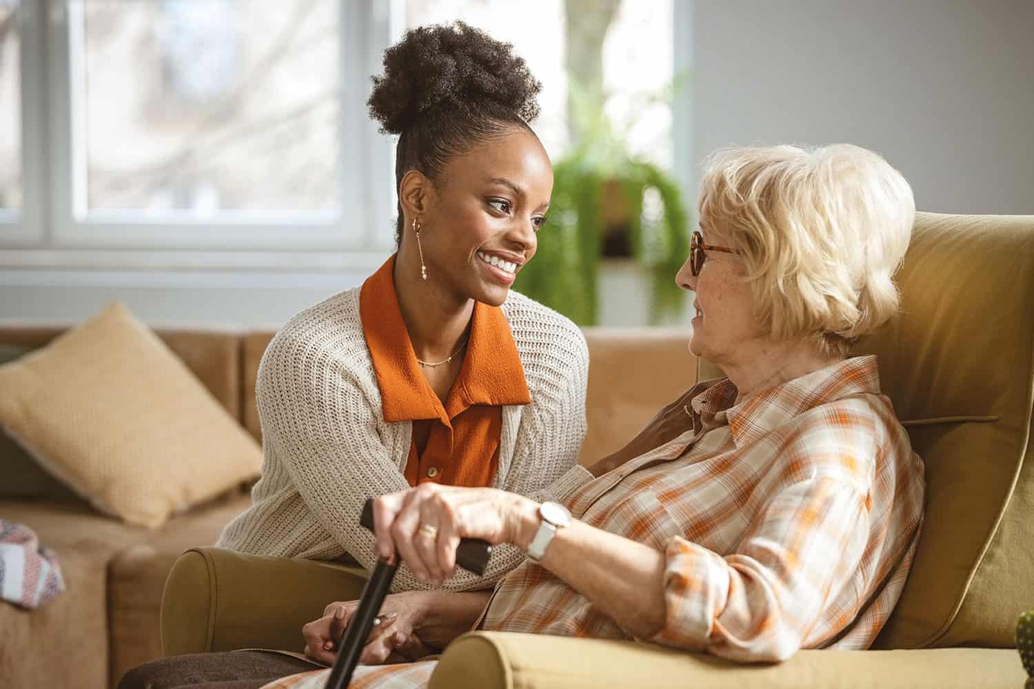 young woman carer with older woman, both sitting on sofa