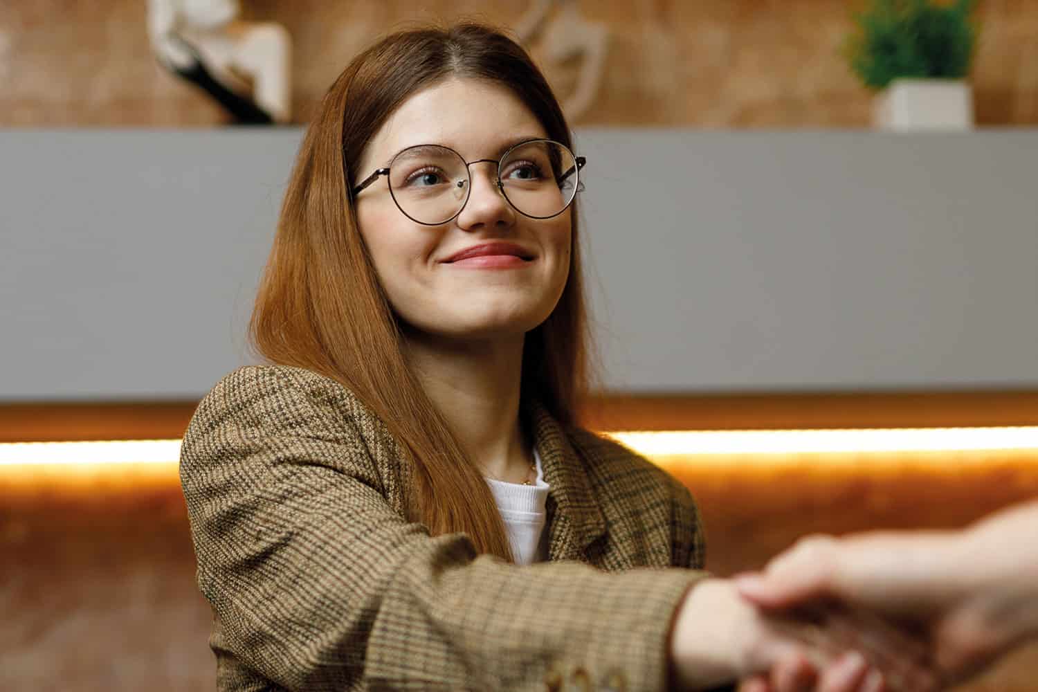young woman seated with arm outstretched to shake hands with someone off camera