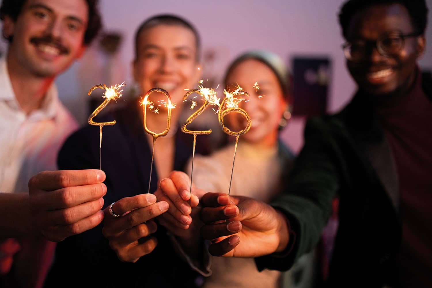 four diverse smiling young people holding up lit sparklers spelling out ‘2026’ – focus on the sparklers