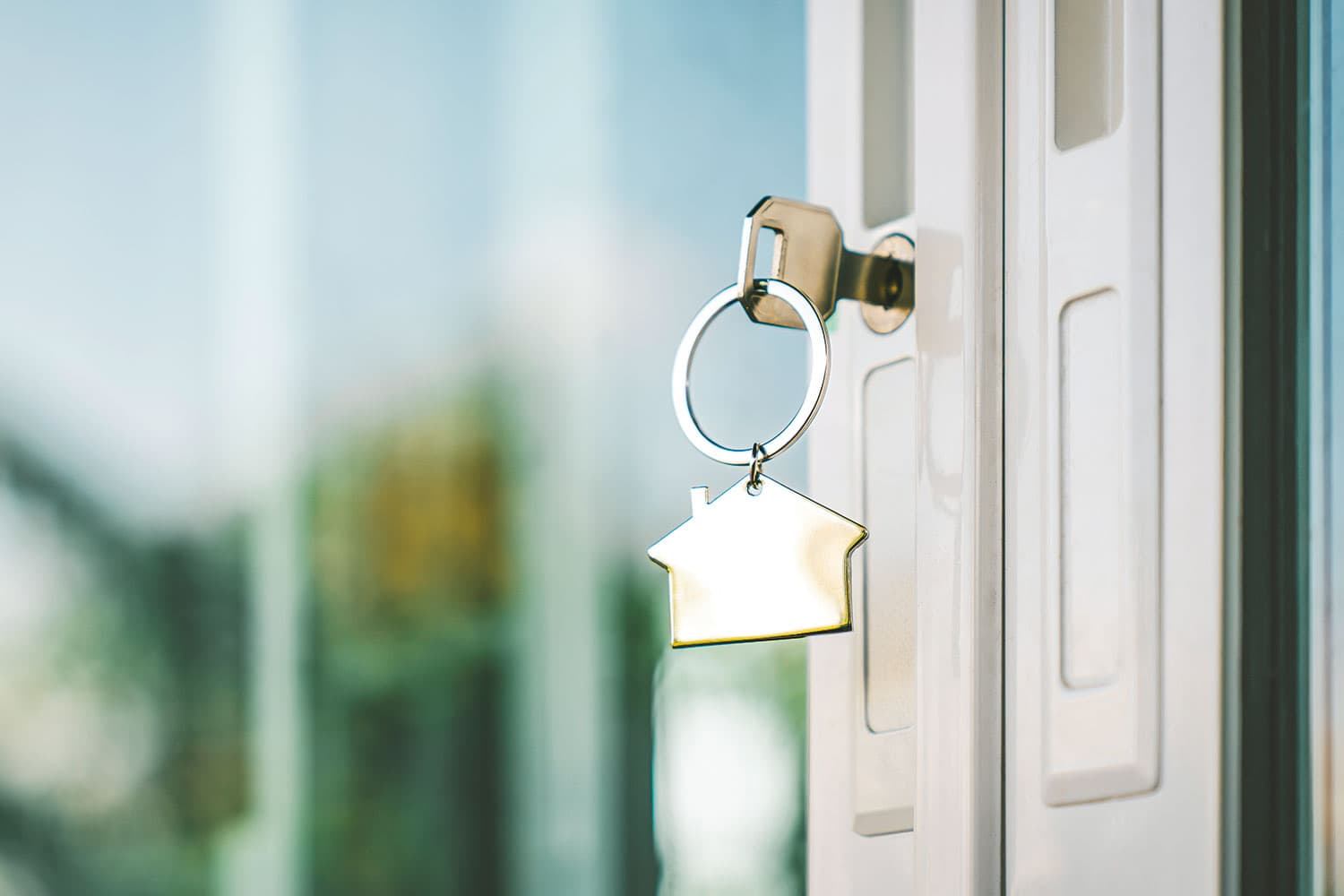 photo, close-up of a key in an white, open front door, with the outline of a house the fob on the keyring