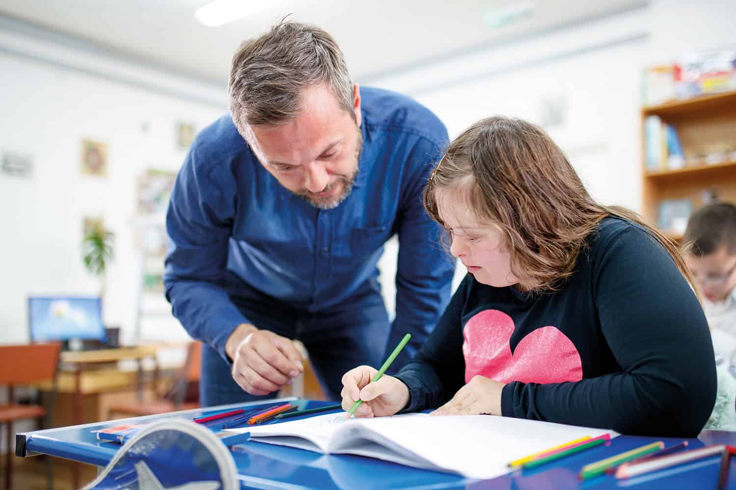 photos of a secondary-age student with special educational needs and disabilities (SEND) drawing or writing in an exercise book with a teacher overlooking from behind