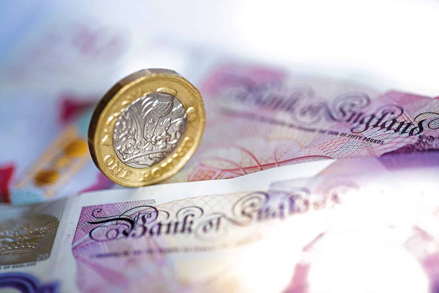 photo of pound coin balanced on its edge on a backdrop of UK sterling bank notes