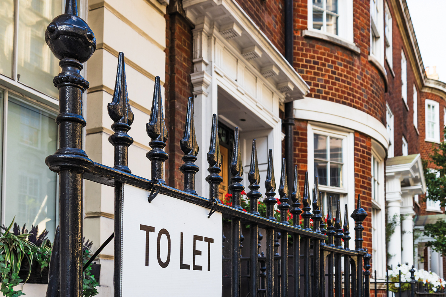 Close up of ‘To let’ sign hanging on rails outside a red-brick house or flats