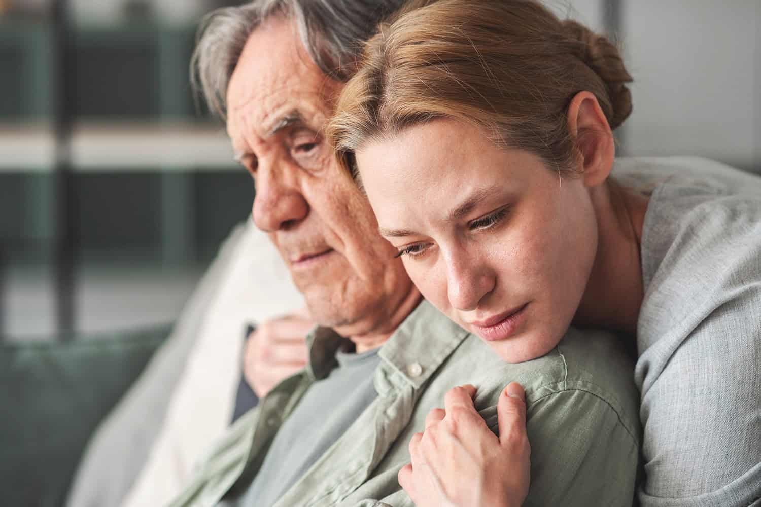 photo of young woman hugging older seated man from behind
