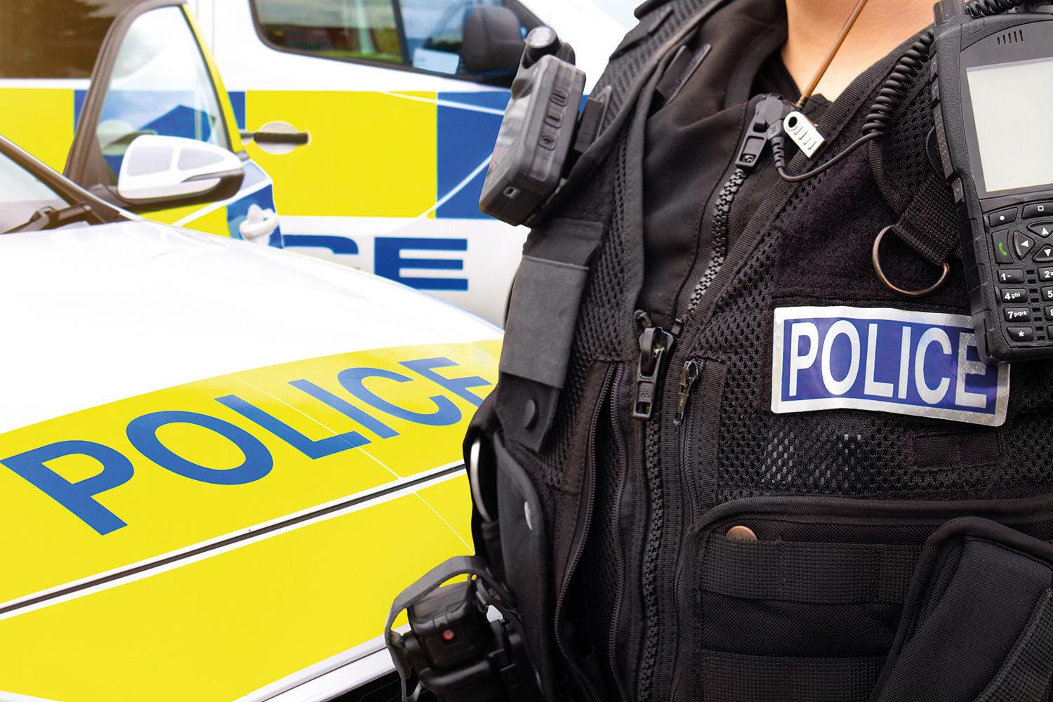 photo of mid-section of uniformed police officer standing next to marked police car