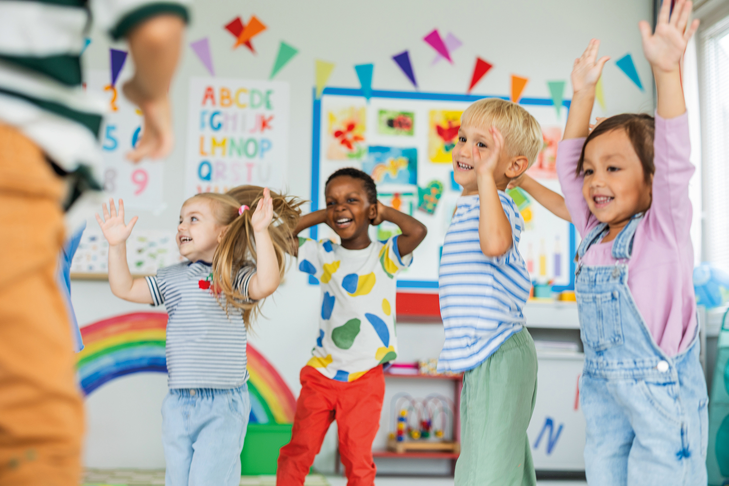 photo of four lively, smiling pre-schoolers jumping up and down in front of a colourful classroom backdrop