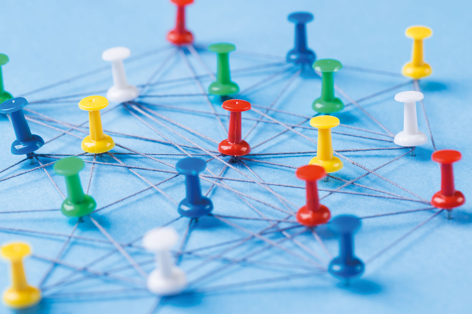 close-up photo of red, blue, green, yellow and white board pins stuck in a light blue board with grey string strung between them in all directions