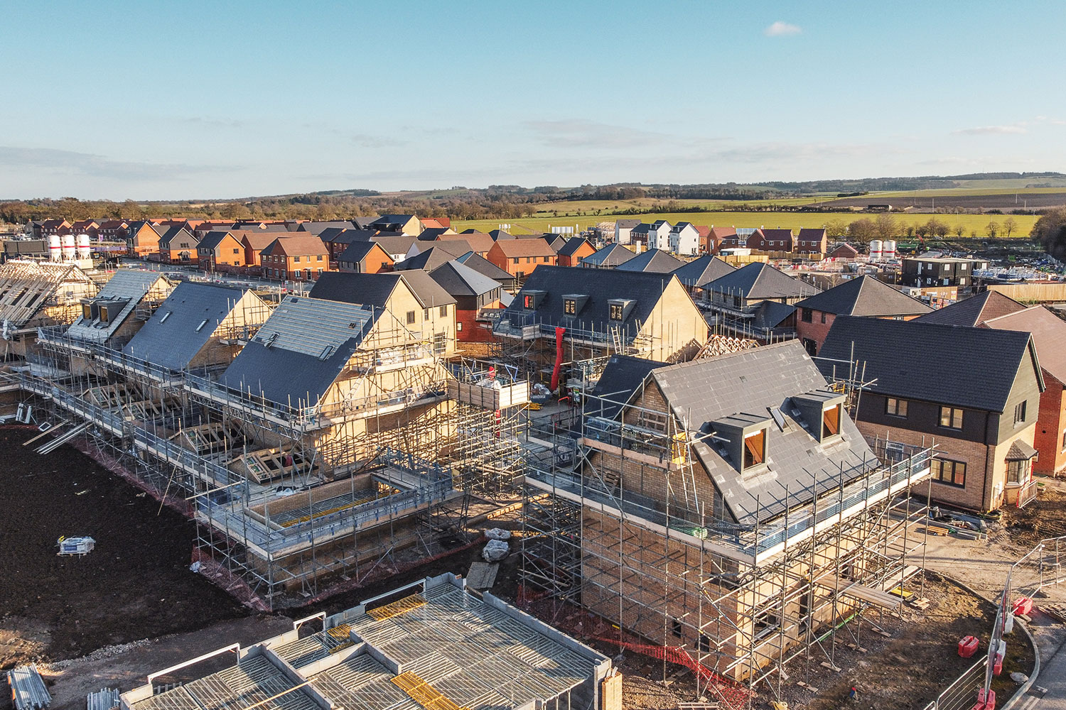 photo from above and to the side of building site with houses in various states of construction with completed new and older housing in the background