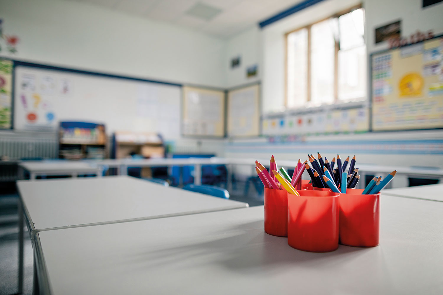 photo of close-up of a pot of pens on an empty school table stretching into an empty classroom