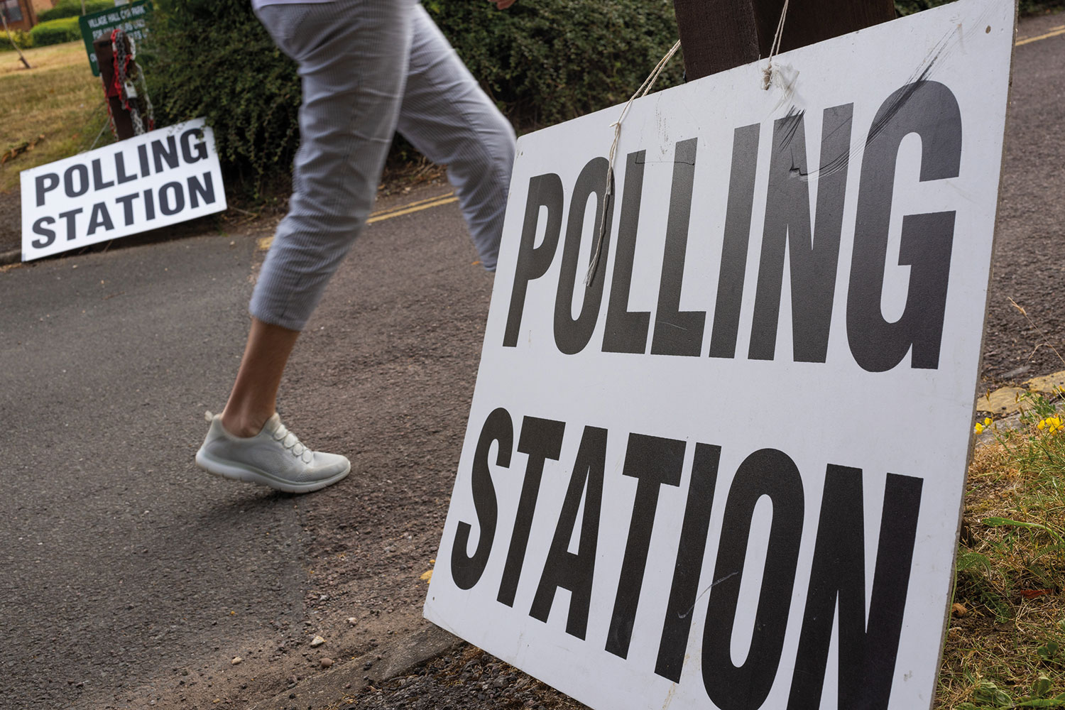 photo of ground-level polling station sign with woman walking past behind it
