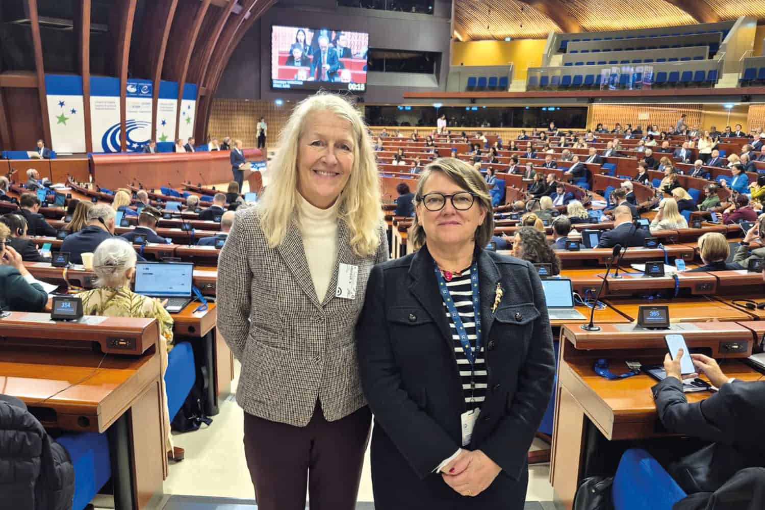 photo of Cllrs Louise Gittins and Bryony Rudkin at the Congress of the Council of Europe – a large hall with semi-circles of desks and members in the background behind them