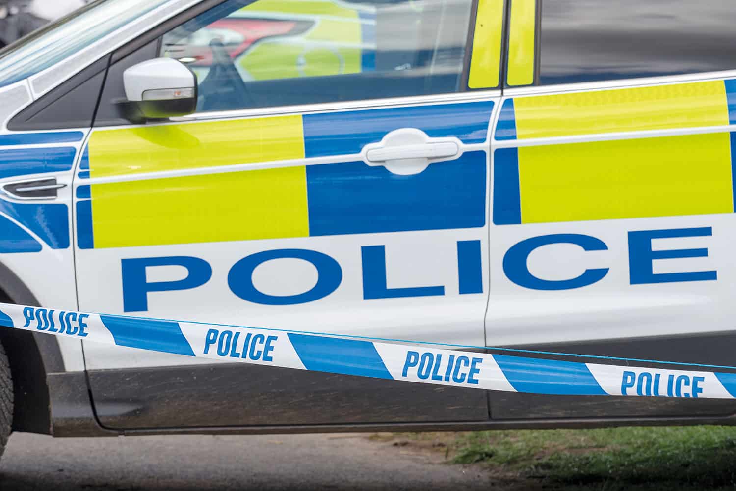 photo of blue ‘police’ tape in front of a police car