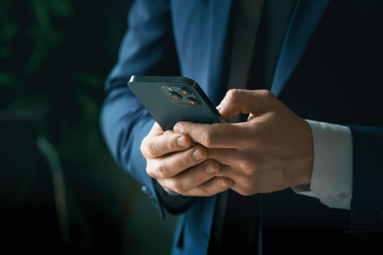 photo of the mid-section of a man in a dark blue shirt, close-up on his hands using a mobile phone