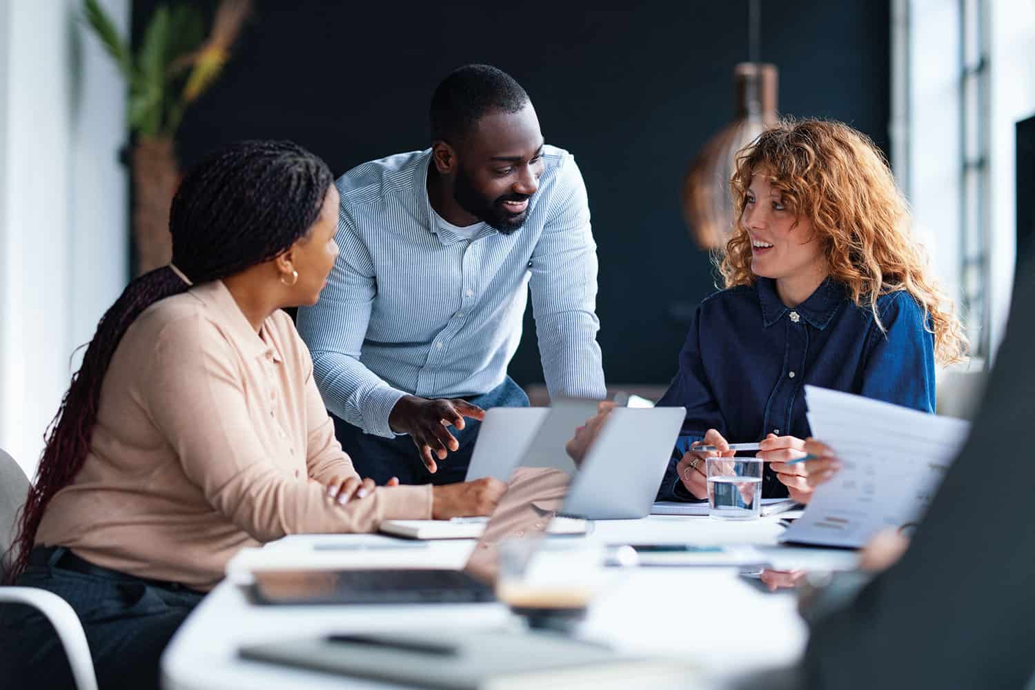 photo of a team of office workers discussing a project over laptops and paperwork