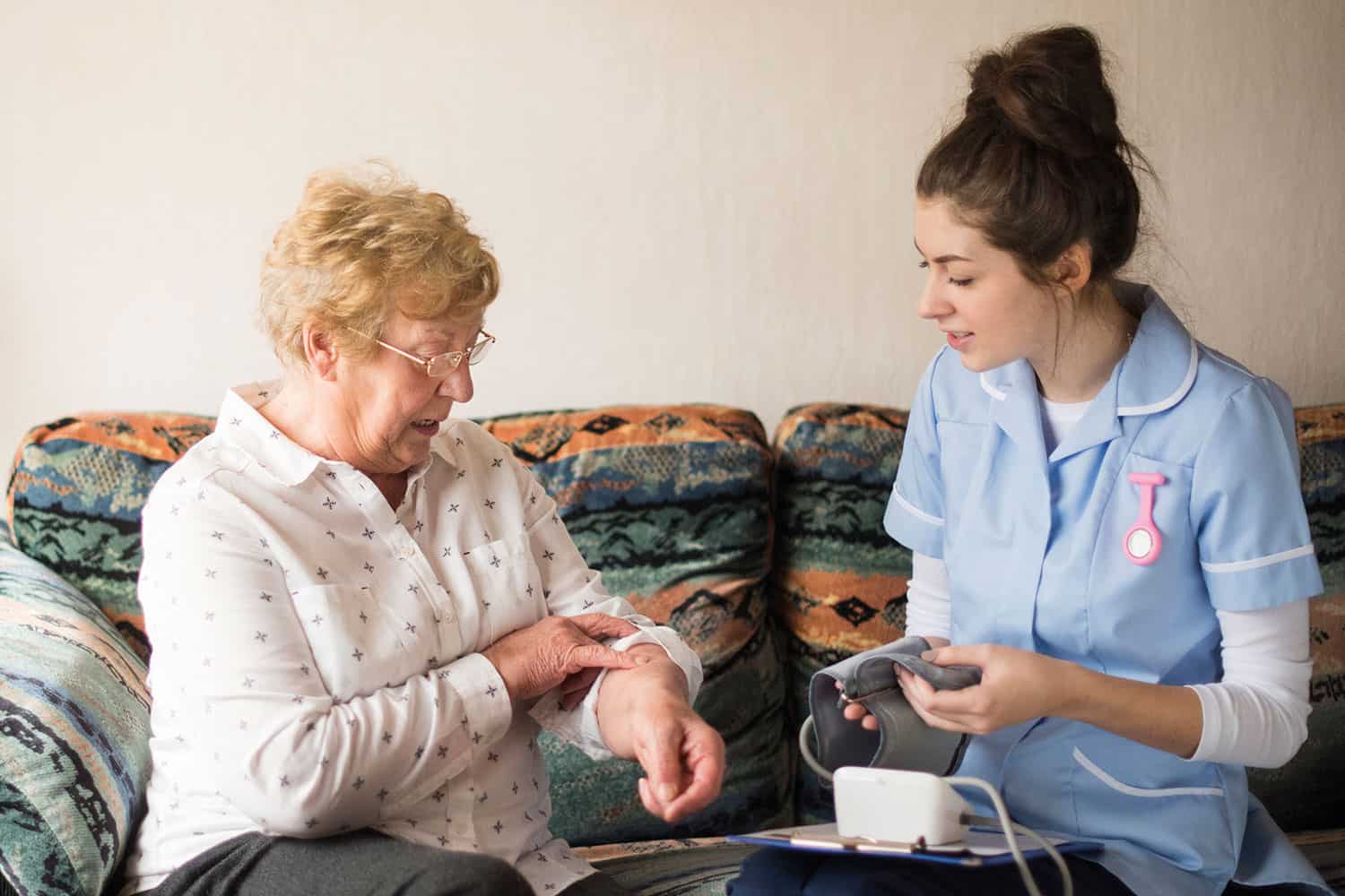 photo of older woman sitting on sofa with nurse on home visit checking meds or taking blood pressure