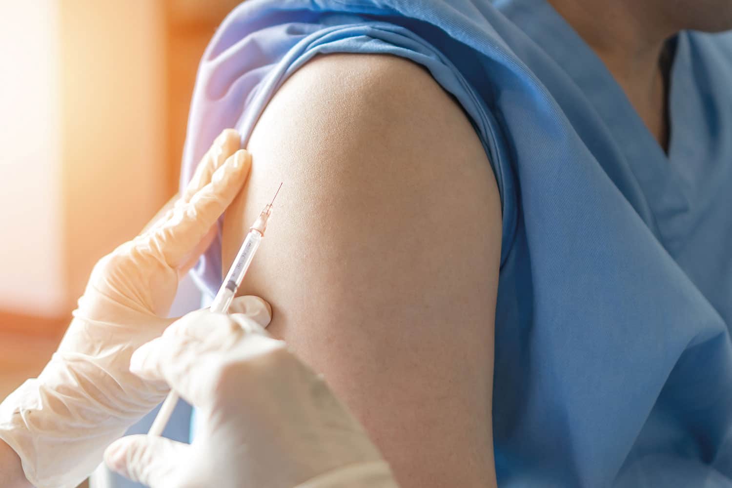 photo of close-up of hands in medical gloves holding a vaccination needle against someone’s upper arm